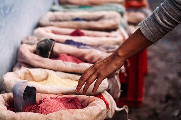 A hand approaches colorful dusty sand bags: Bags of vibrant, colorful sand invite creative exploration and sensory delights.