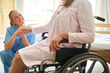 Nurse holding hand of senior woman in wheelchair at rehab center
