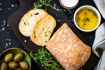 Ciabatta bread with olive oil, olives and herbs on black. Mediterranean food. Top view.