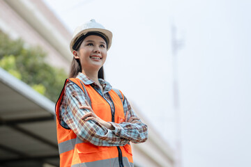 Asian engineer beautiful woman or architect looking forward with white safety helmet in construction site. Standing at modern building construction. Worker asian woman working project building