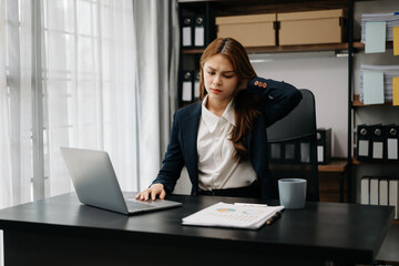 Overworked young Asian businesswoman office worker suffering from neck pain after had a long day at her office table. office syndrome concept