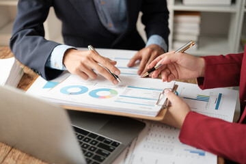 Team of two asian male and female business people working together discussing new financial graph data on office table with laptop and digital tablet.