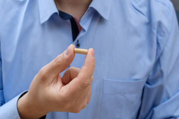 Mężczyzna w niebieskiej koszuli trzymający kapsułkę z lekiem
