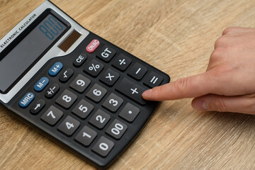 Mężczyzna liczący wydatki na kalkulatorze, który leży na biurku  - obrazy, fototapety, plakaty