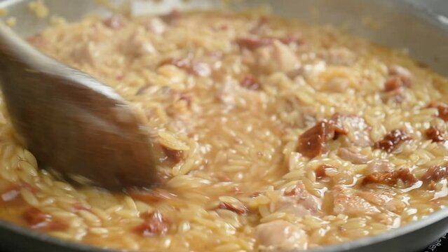 Preparing chicken with orzo pasta in a frying pan.
