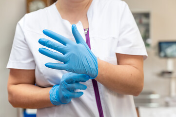 Close up of a nurse putting a blue latex gloves on a clinic background. High quality photo
