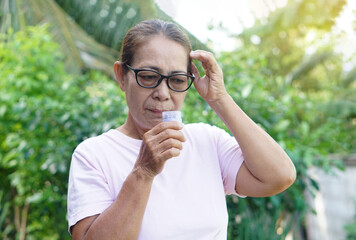 Asian senior woman holds bottle of Thai herbal inhaler to smell to relieve dizzy symptoms. Concept,...