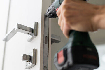 A locksmith is repairing an interior door lock. Close-up of male hands repairing or replacing an entrance door lock with a hex screwdriver