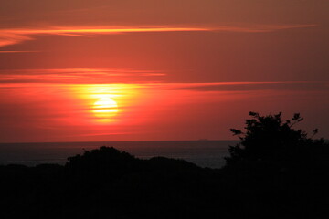 at the sea the red-golden sun shines out from behind the clouds before it sets