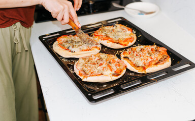 Homemade mini pizza on a baking sheet, hand cutting traditional italian food with a knife selective focus