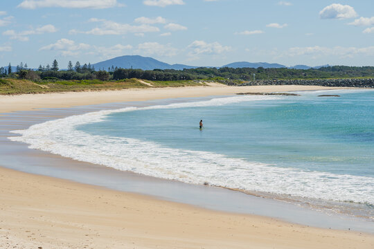 A solitary swimmer standing in a shallow ocean bay with a white sand beach