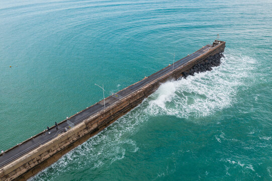 Aerial view of a wave crashing against a long narrow breakwater