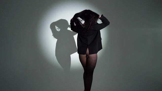 A brunette business girl in black underwear and a business black jacket with a beautiful athletic figure poses in a dark studio with light, in pantyhose