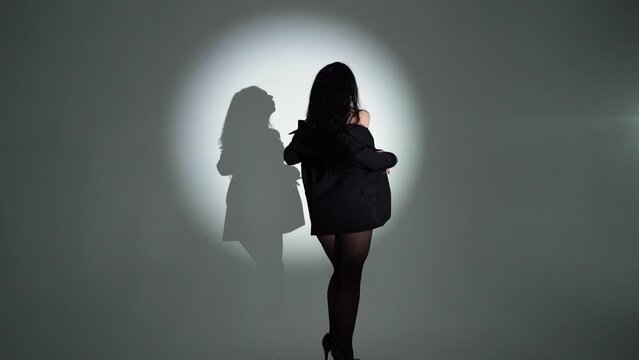A brunette business girl in black underwear and a business black jacket with a beautiful athletic figure poses in a dark studio with light, in pantyhose