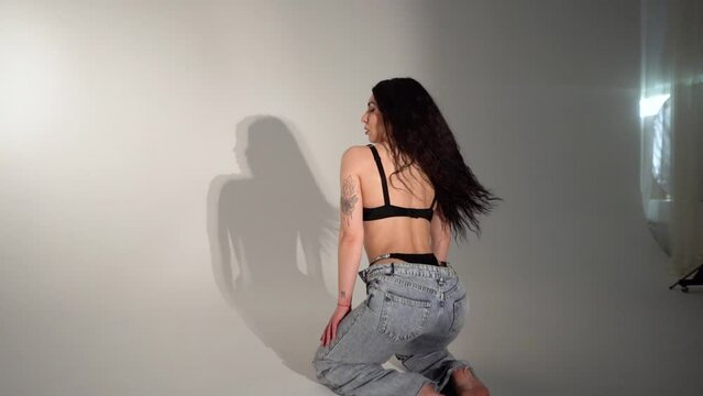 Brunette girl in lingerie and jeans with a beautiful athletic figure posing in a dark studio with light