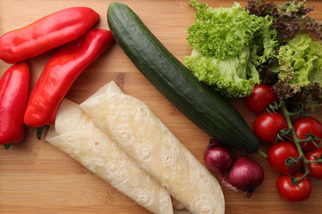 Cucumber, tomatoes, onions, peppers, salad leaf, wraps on a wood table