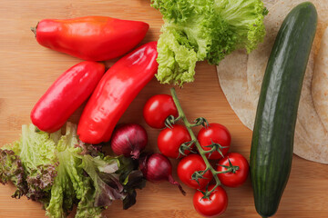 Cucumber, tomatoes, onions, peppers, salad leaf, wraps on a wood table