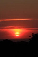 Obraz premium at the sea the red-golden sun shines out from behind the clouds before it sets