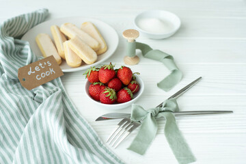 On the table are kitchen utensils and a plate with a fresh harvest - strawberries, a plate with Savoyard cookies. Next to it is the inscription let's cook