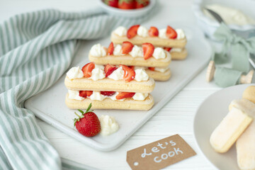 The process of making a dessert of Savoyard cookies, strawberries and buttercream. The photo is part of a group of photos where the creation of the dessert is shown step by step