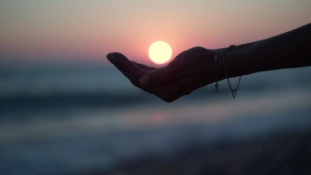 Side view silhouette of female hand holding red sun in palm in twilight darkness. Closeup unrecognizable Caucasian woman in dusk on Mediterranean sea shore on Cyprus