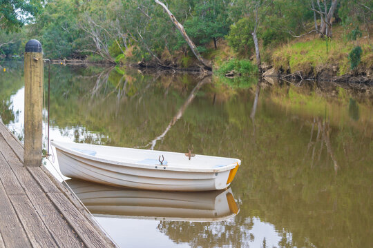 A solitary row boat tied to a bollard alongside a dock on a still river