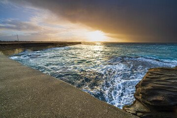 A dramatic sunrise with a dark cloud bank over a coast breakwater wall