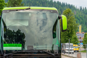 Close-up of a large windshield of a tourist bus at a bus stop, blurred background of green trees and buses, reflections of clouds and trees in the glass of the bus, summer travel - Powered by Adobe