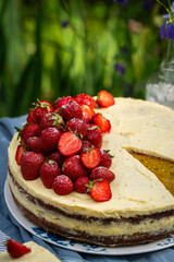Fresh strawberries on top of homemade sponge cake with custard on wooden cake stand  in blooming garden.