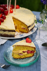 Slice of homemade strawberry cake on wooden cake stand on round table in blooming garden.