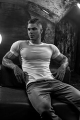 Athletic man in white t-shirt tight sexy abs sitting on a leather sofa