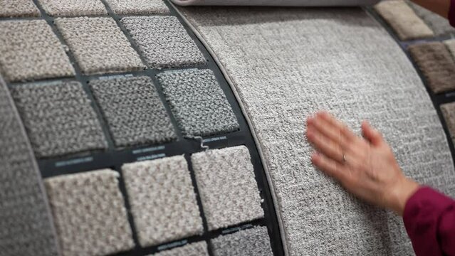 Mature woman runs hand over carpet samples shopping in large hardware store for home renovation project.