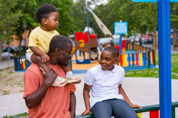 Fototapeta na wymiar African black ethnicity father talking with his children in the playground of the city park
