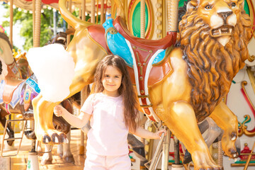 Little girl with cotton candy in an amusement park. The concept of summer holidays and school holidays