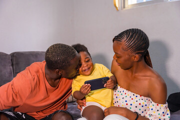 African black ethnicity family with their son on the sofa at home smiling and having fun with the phone