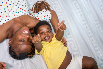 Fototapeta na wymiar African black ethnic family mother with her little son in bedroom on bed smiling, overhead shot