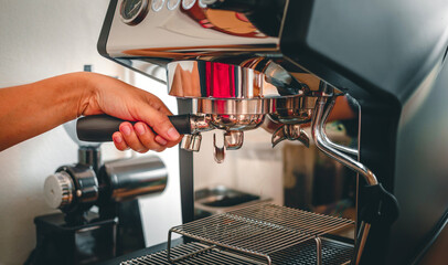 Hand of a barista holding a portafilter barista working making coffee with a coffee machine in coffee shop