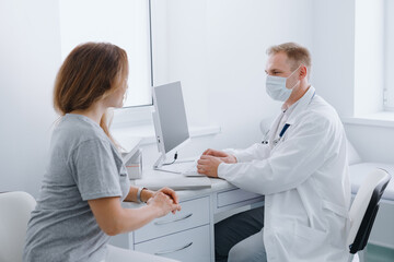 Fototapeta premium A doctor in a protective mask receives a patient in his office. Prevention of diseases during a pandemic.