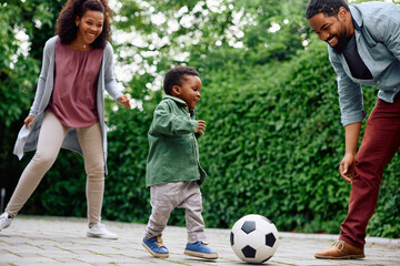 Happy black boy and his parents play with ball in backyard.