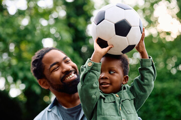 Happy black boy holds ball while playing with his father outdoors.