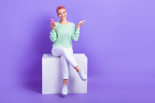 Full length photo of cute sweet lady dressed teal pullover typing modern device pointing empty space isolated purple color background