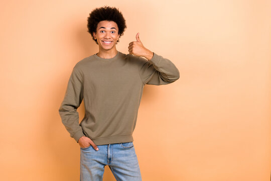Photo of young optimistic guy chevelure hair thumb up wear stylish pullover thumb up like new clothes brand advert isolated on beige color background
