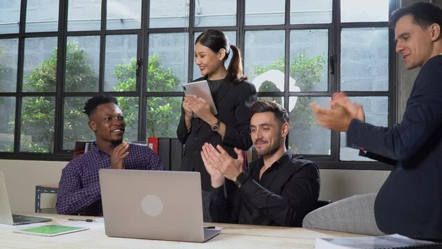 group of happy multi-ethnic business people meeting with laptop computer on table excited and clapping hand together to success in office. diversity team building young worker discussion together.