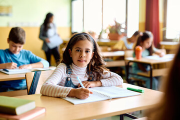 Hispanic schoolgirl writing during class in classroom and looking at camera.