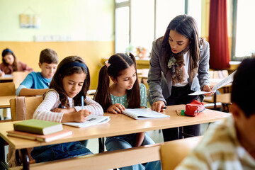 Hispanic teacher assists her students with their assignment during class at school.