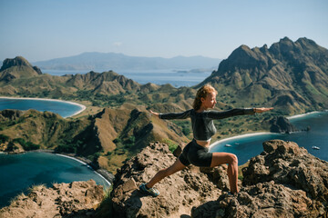 A beautiful young girl doing yoga on top of a mountain overlooking Padar Island, Indonesia.