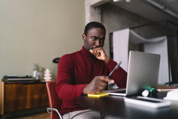 Fototapeta na wymiar Thoughtful African American man with pen working on laptop