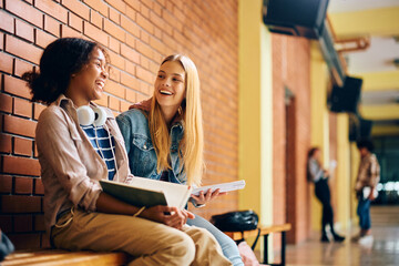 Happy female high school students laugh while learning in hallway.
