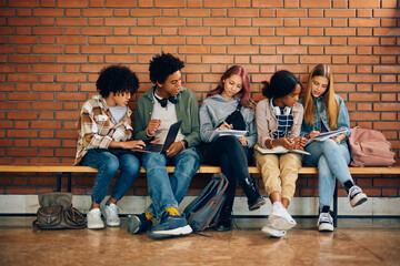 Multiracial group of teenagers studying together in high school hallway.