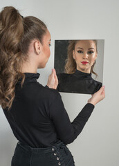 Attractive woman in black blouse and red lips  look into the mirror in front of a background. boudoir scene.  Sensual young  woman with long curly hair and black jeans wearing in front of camera